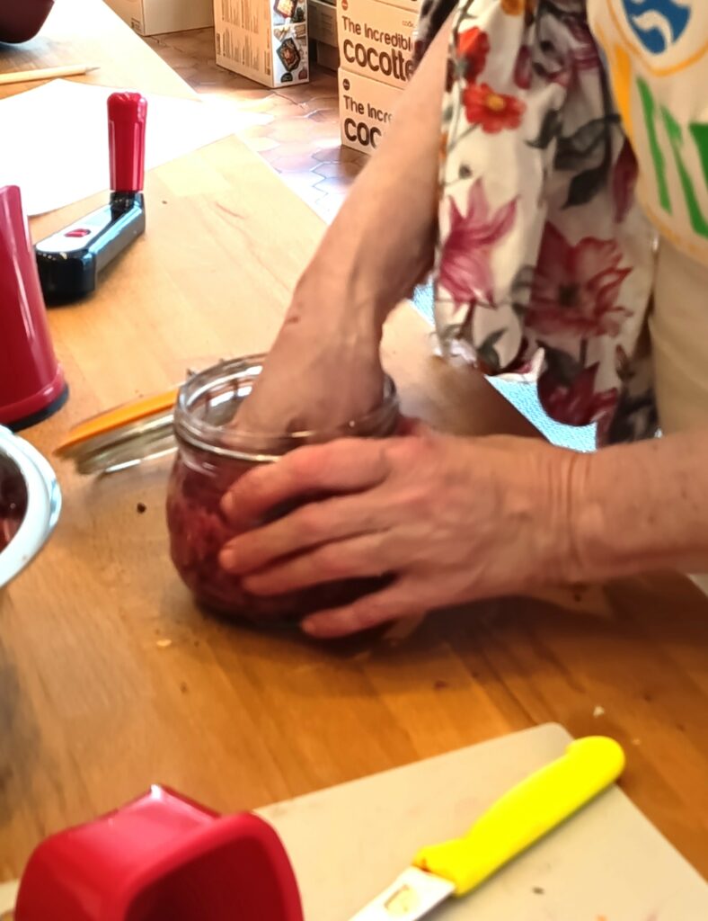 Participante tassant les légumes dans le bocal de 500 ml pour la préparation de lactofermentation lors de l'atelier animé par alyferm à Fécamp au coup de pâte d'isa le 7 mai 2026